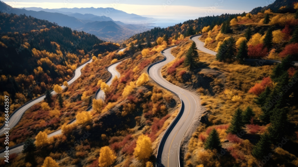 Aerial view over winding road on a mountain top with trees by autumn.