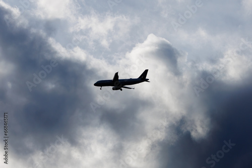 Silhouette of an airplane with its landing gear coming down ready to land with a cloudy background