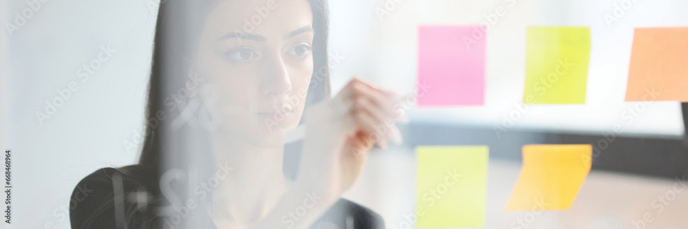 Fototapeta premium Woman creates business plan putting sticky notes on wall