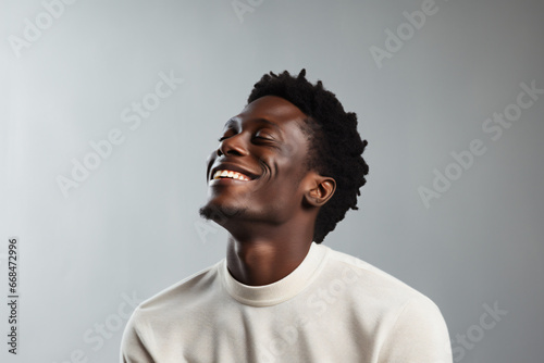 Closeup of young black man with head tilted up smiling with eyes closed on a white background. Minimalist image. Harmonies of luminous colors. Sincere and natural photography. Copy space.