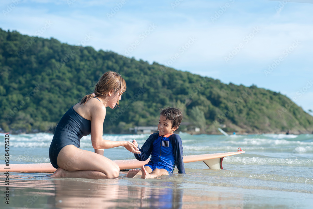 Mother and son sits on the beach and rests after surf, lifestyle activities, water sports