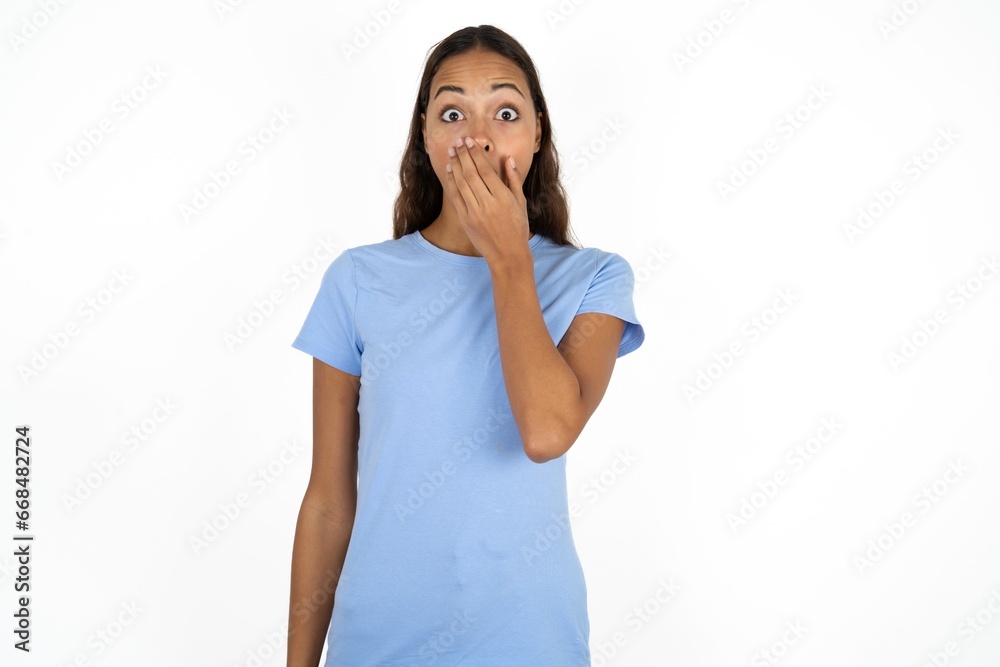 Emotional Beautiful girl wearing blue T-shirt gasps from astonishment, covers opened mouth with palm, looks shocked at camera. Emotional Beautiful girl wearing blue T-shirt gasps from astonishment, covers opened mouth with palm, looks shocked at camera.