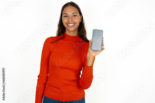 Smiling Beautiful girl wearing red sweater Mock up copy space. Hold mobile phone with blank empty screen