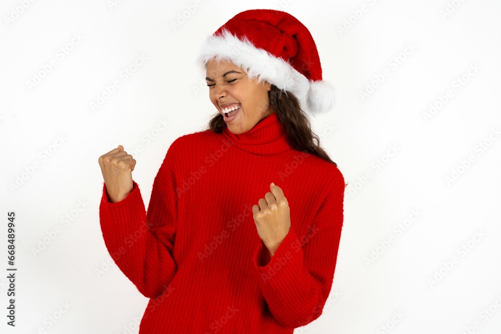 Beautiful woman wearing christmas hat very happy and excited doing winner gesture with arms raised, smiling and screaming for success. Celebration concept.