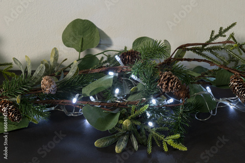 Christmas Garland Decoration, Lush Greenery, Pinecones, and Silver LED Lights on Dark Surface, Twinkling Amidst Eucalyptus Leaves and Spruce Twigs, Festive Holiday Ornament for Home Interiors. © JesusCarreon