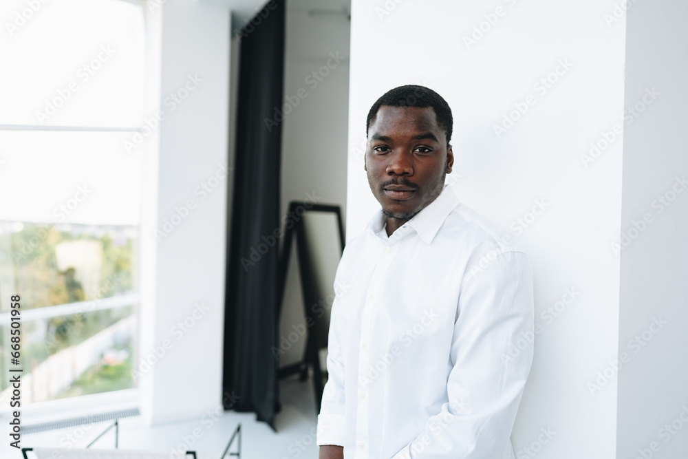 Young african man in white shirt and glasses posing near large window