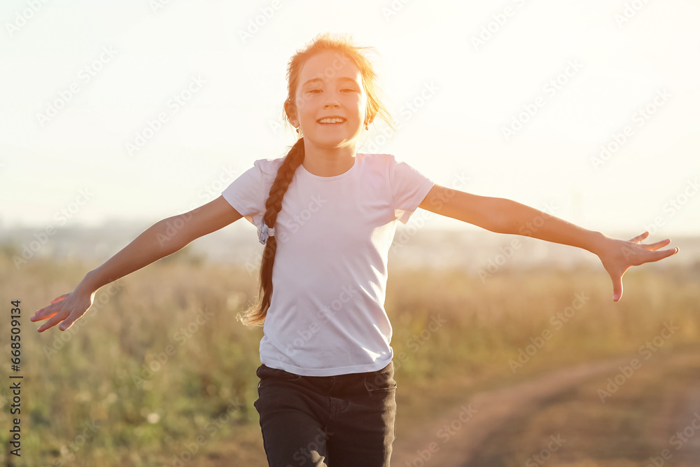 Cheerful girl runs along road in field with outstretched arms imitating airplane. Concept of fun and active movement overlooking beauties of nature, sunlight Cheerful girl runs along road in field with outstretched arms imitating airplane. Concept of fun and active movement overlooking beauties of nature, sunlight