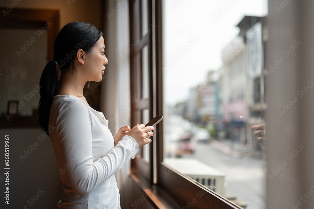 Side view of a thoughtful Asian woman is looking out the window, and thinking something in her mind.