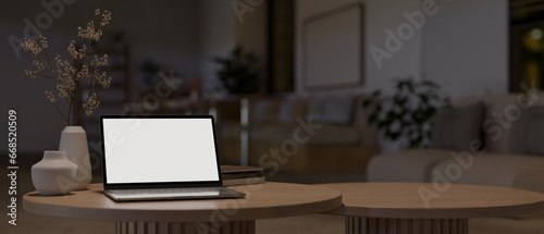 A laptop mockup on a minimal wooden coffee table in a modern and cosy home living room at night.