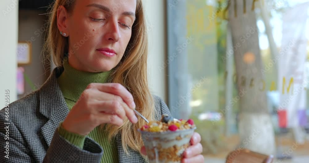 Woman eating natural organic berry smoothie bowl with various nuts in vegan cafe