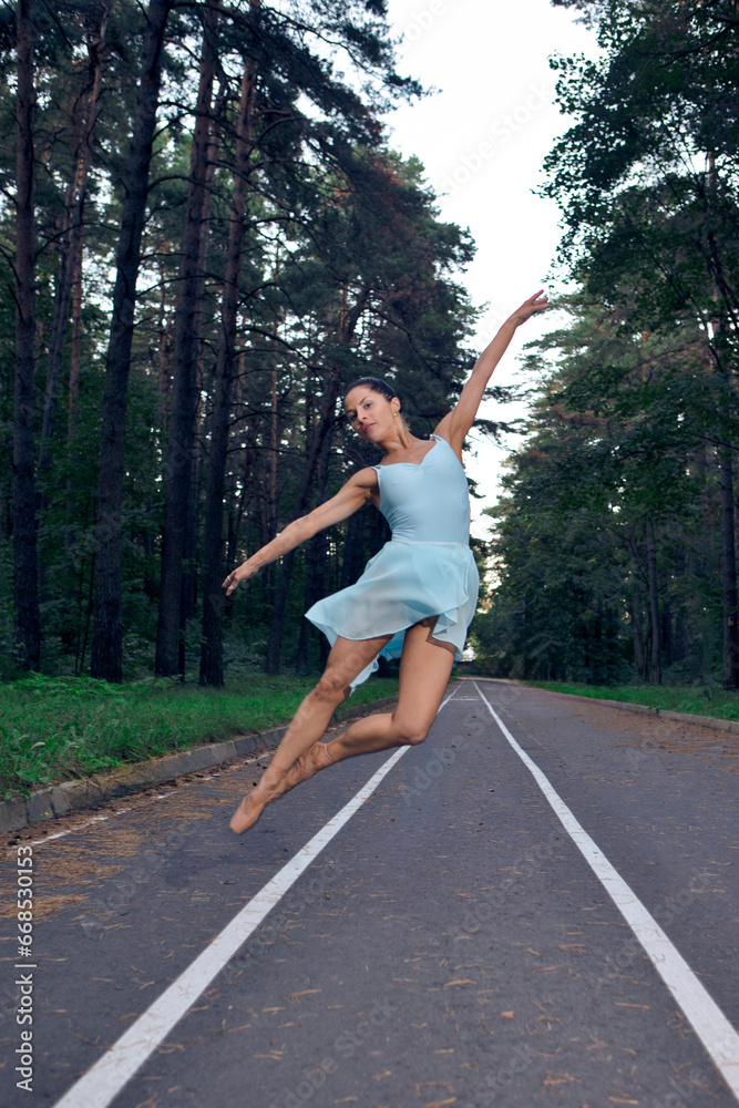 Sexy Slim Young Caucasian Ballet Dancer in Light Blue Tutu Posing in Jumping Dance Pose During Ballet Pas in Summer Forest With Lifted Hands