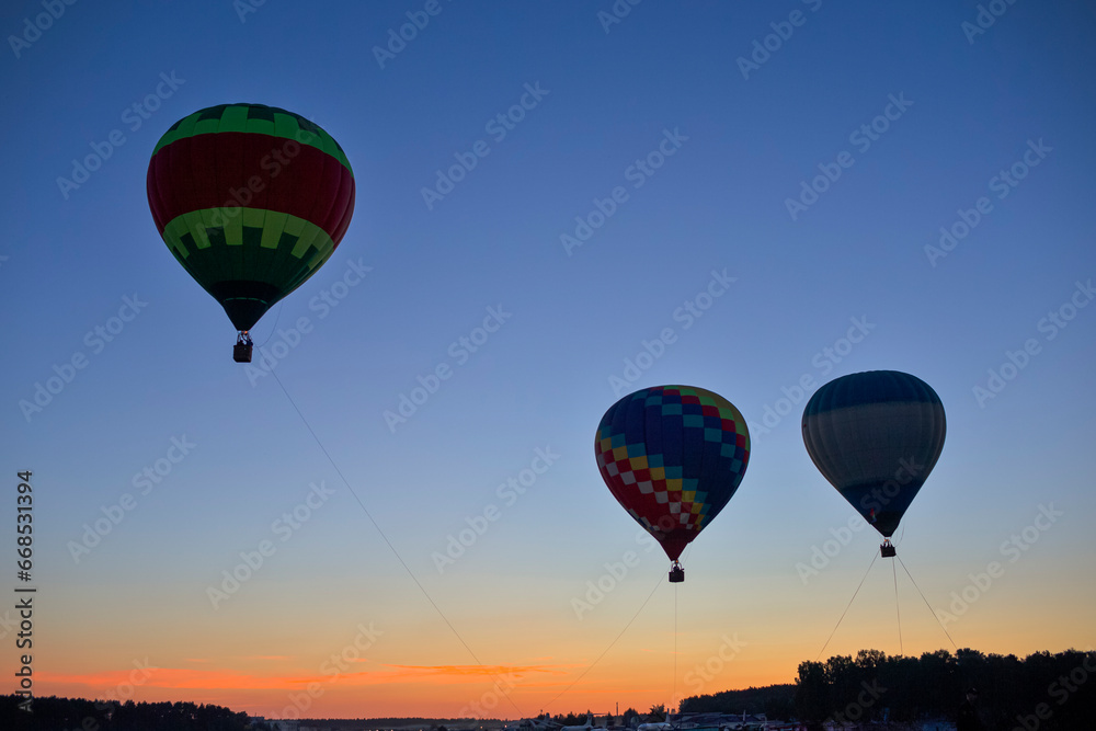 Fototapeta premium Three Amazing Colorful Air Balloons Levitating Over the Ground Outdoors Against Clear Blue Skies