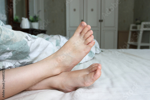 Feet under a light blanket on the bed. Concept of health