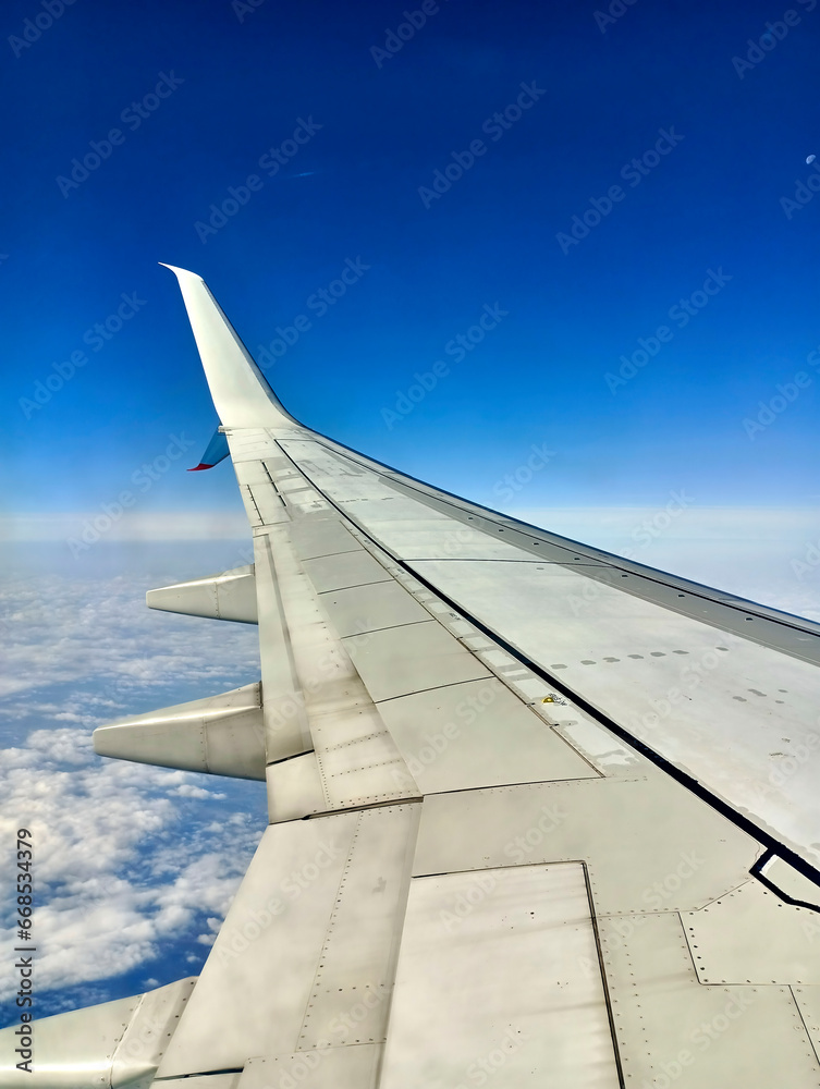 View over the Wing of a Passenger Aircraft from High Altitude on the Clouds in the Blue Sky beneath the Aircraft View over the Wing of a Passenger Aircraft from High Altitude on the Clouds in the Blue Sky beneath the Aircraft