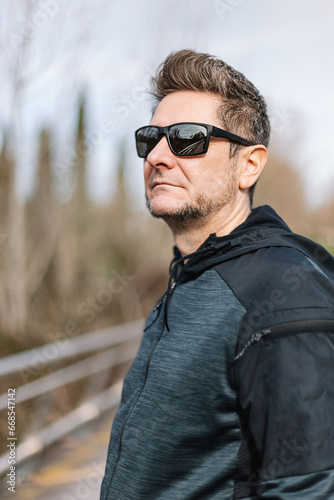 Portrait of a 45-50 years old man with sport clothes, sunglasses and toupee in exterior. Concept of relaxation after sports, confidence and self-confidence.