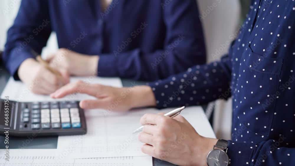 Two accountants dressed in blue are using calculator for counting taxes at grey desk in office, front side view. Teamwork in business audit and finance Two accountants dressed in blue are using calculator for counting taxes at grey desk in office, front side view. Teamwork in business audit and finance