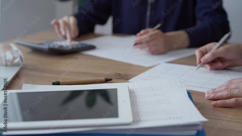 Two accountants are using a laptop computer and calculator for counting taxes at a wooden desk in office. Teamwork in business audit and finance Two accountants are using a laptop computer and calculator for counting taxes at a wooden desk in office. Teamwork in business audit and finance