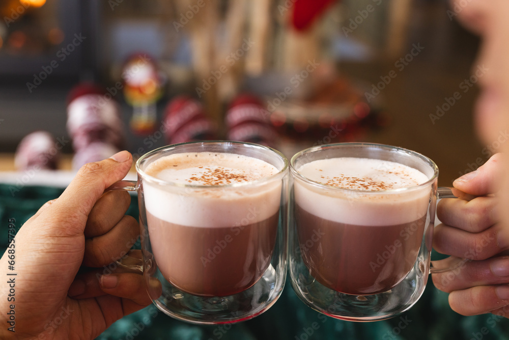 Diverse gay male couple holding glasses of cocoa and wearing christmas clothes at home Diverse gay male couple holding glasses of cocoa and wearing christmas clothes at home