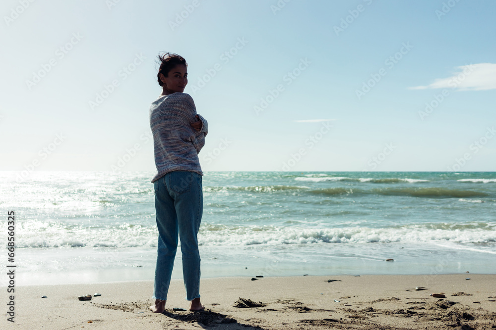 A beautiful brunette girl stands barefoot on the sandy seashore, enjoying the nature A beautiful brunette girl stands barefoot on the sandy seashore, enjoying the nature