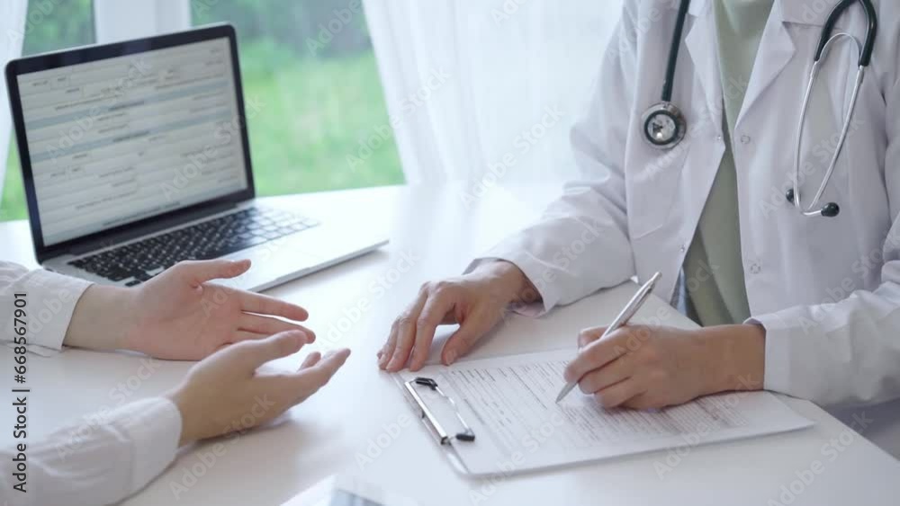 Doctor and patient sitting at the white table in the hospital. The pediatrician in a green blouse and white medical coat is listening to a woman and writing notes on a clipboard. Medicine and Doctor and patient sitting at the white table in the hospital. The pediatrician in a green blouse and white medical coat is listening to a woman and writing notes on a clipboard. Medicine and