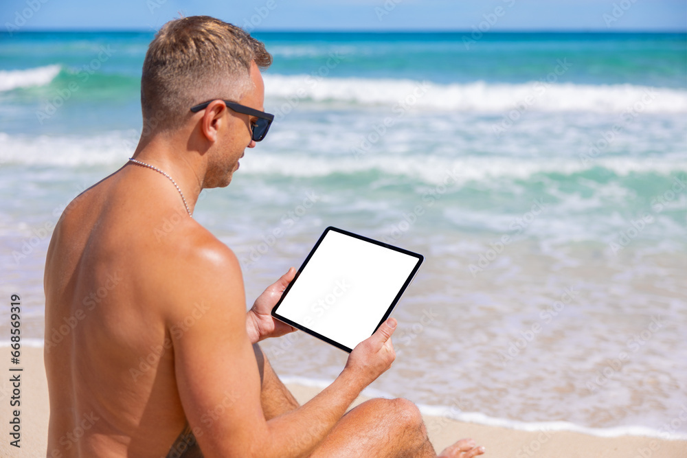 Man relaxing on the beach and holding tablet computer with empty white screen