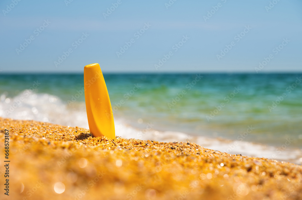 Sunscreen in the sand against the background of the sea. Yellow tube of sun skin care product without label. Mockup for your brand Sunscreen in the sand against the background of the sea. Yellow tube of sun skin care product without label. Mockup for your brand