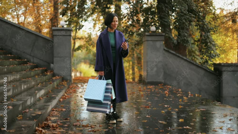 Interesting happy middle-aged woman using phone, reading good news, smiling, walking on city street in autumn park. Good mood. Portrait. Slow motion Interesting happy middle-aged woman using phone, reading good news, smiling, walking on city street in autumn park. Good mood. Portrait. Slow motion
