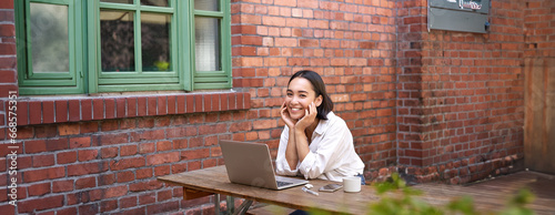 Beautiful brunette woman sitting outdoors and using laptop, chatting online, working with computer outside office photo