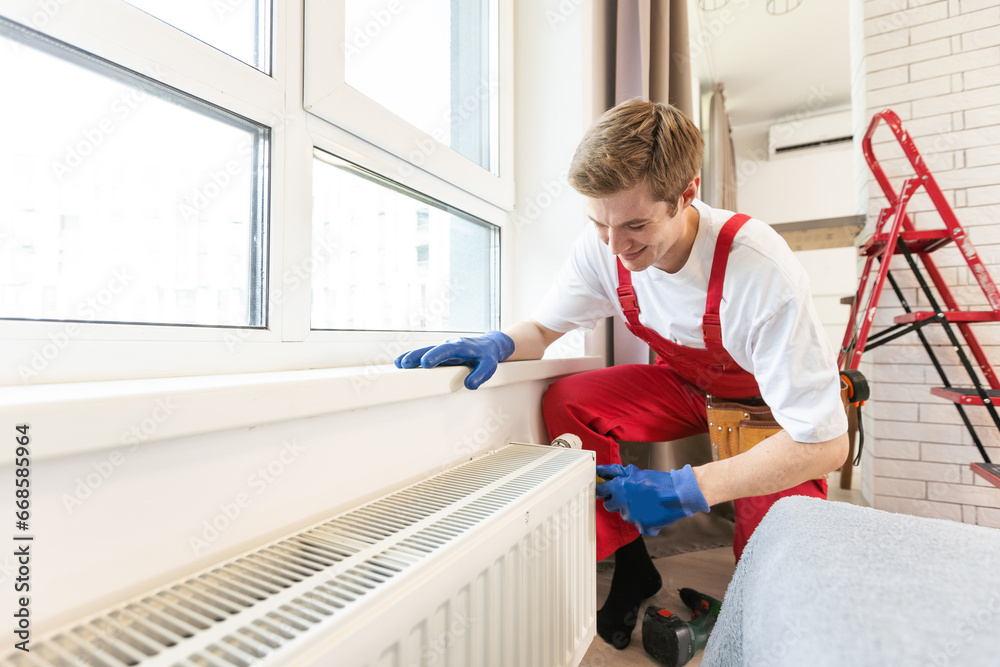 Full length shot of two professional plumbers, workers in uniform fixing or installing heating radiator. Construction, maintenance and repair concept. Full length shot of two professional plumbers, workers in uniform fixing or installing heating radiator. Construction, maintenance and repair concept.