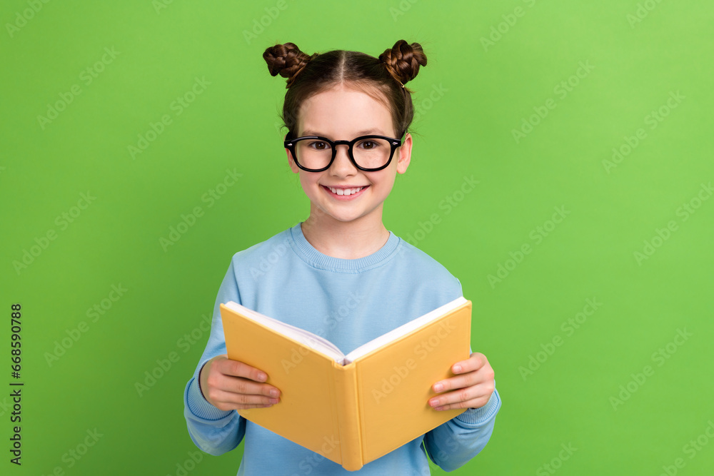 Portrait of adorable small girl with brown hair wear blue sweatshirt in eyewear hold book at lesson isolated on green color background Portrait of adorable small girl with brown hair wear blue sweatshirt in eyewear hold book at lesson isolated on green color background