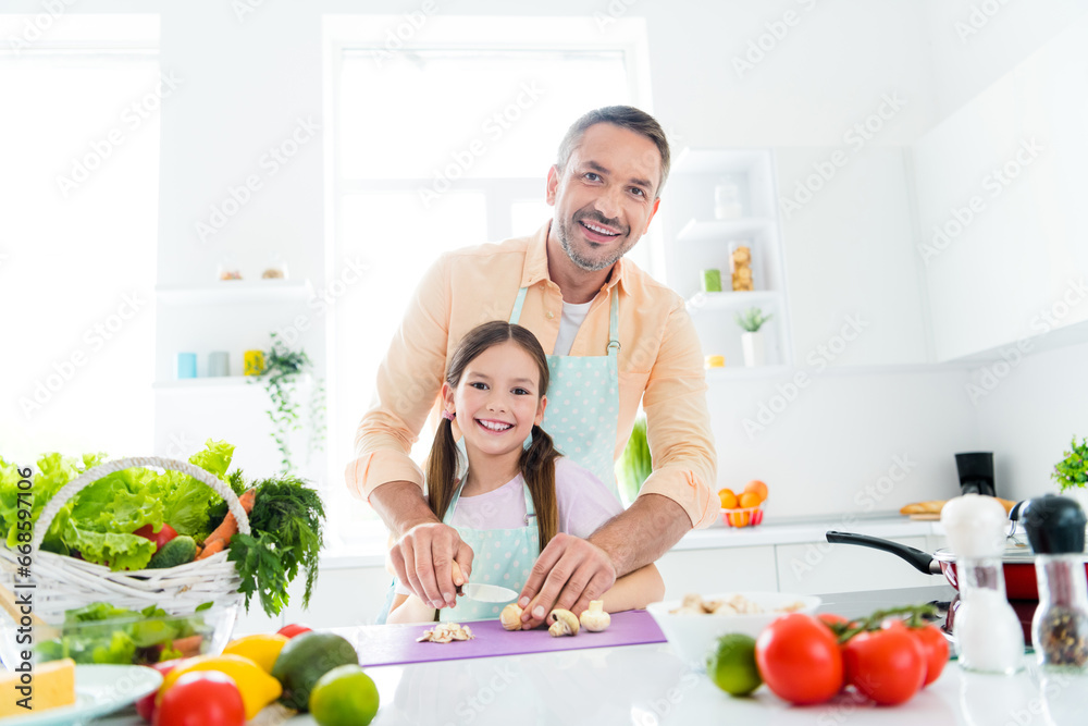 Photo of sweet excited father little girl cutting vegetables preparing lunch together indoors apartment kitchen