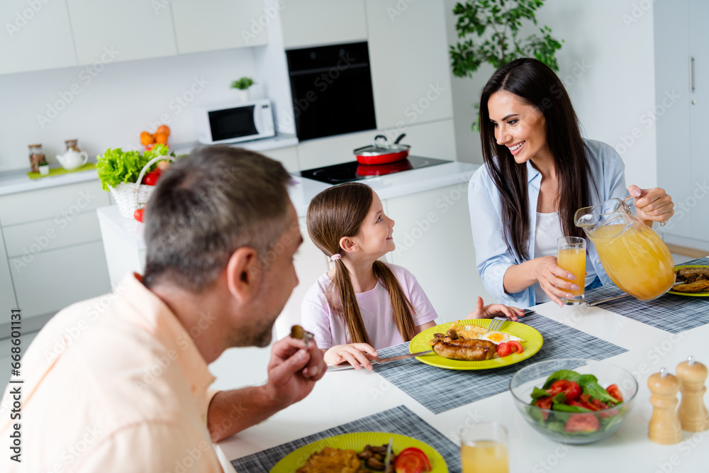 Photo of cheerful parents communicate pour fresh juice small daughter domestic food plate serenity house kitchen inside