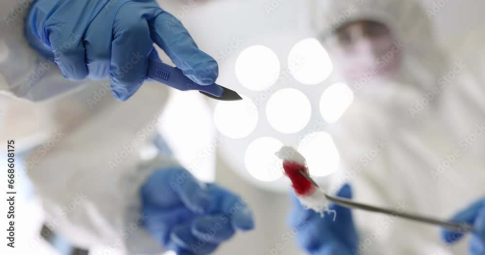 Two surgeons in protective suits hold scalpel and cotton pad with blood over a patient. Surgical operations concept