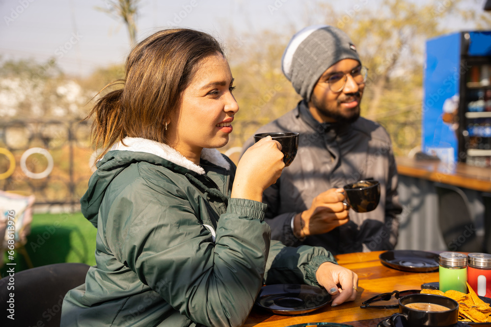 Fototapeta premium Happy young indian friends wearing winter cloths having a coffee together in cappuccino restaurant. Life style concept with happy men and women at cafe terrace.
