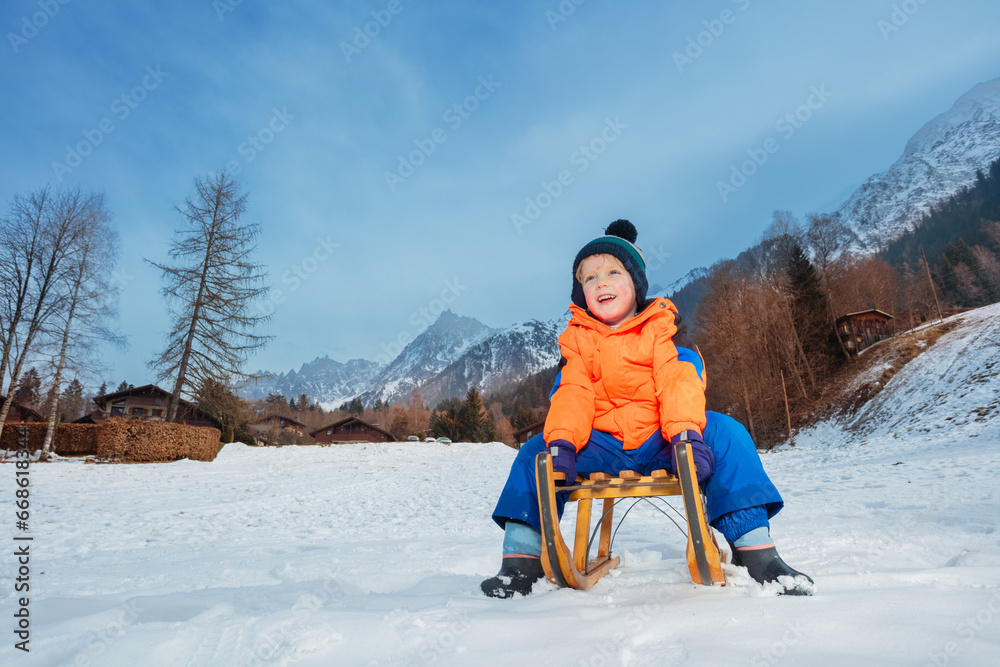 Boy in winter outfit sit on the sledge about to slide downhill