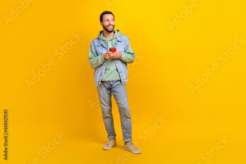 Full body length photo of young latin guy boyfriend male hold phone thinking glovo delivery look mockup isolated on yellow color background