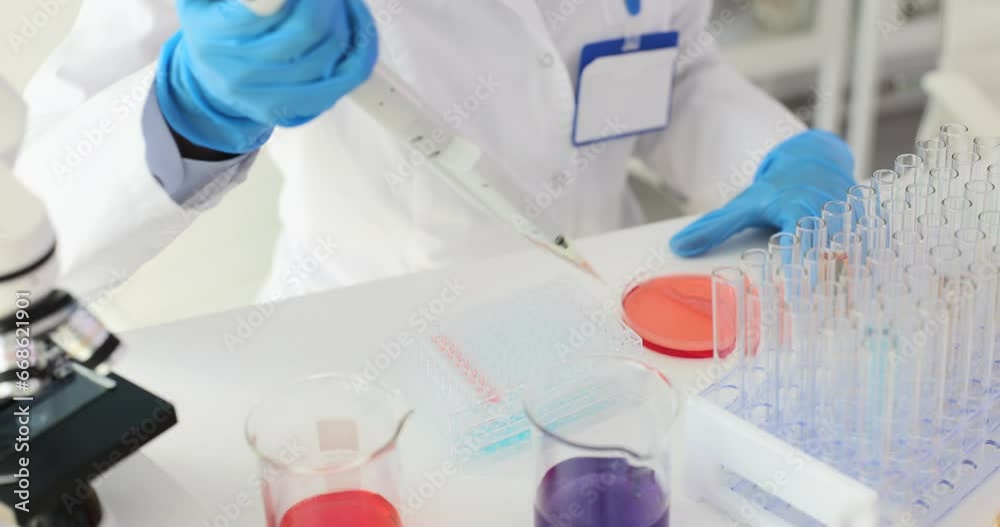 Doctor or scientist uses mechanical pipette to add fluid samples to special transparent container. Microbiological research and work in scientific laboratory Doctor or scientist uses mechanical pipette to add fluid samples to special transparent container. Microbiological research and work in scientific laboratory