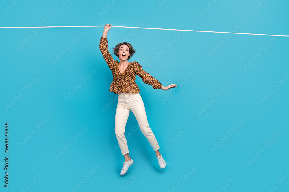 Photo of surprised lady hanging on rope playing incredible extreme sport game isolated blue color background - obrazy, fototapety, plakaty 