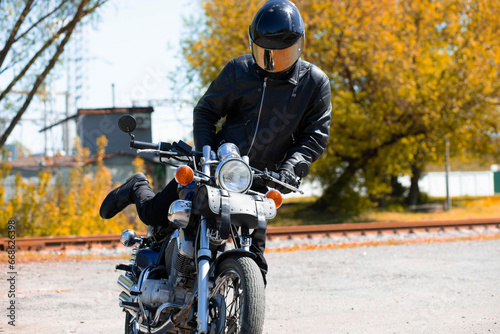 motorcyclist biker in a leather jacket and helmet on a classic chopper motorcycle in autumn