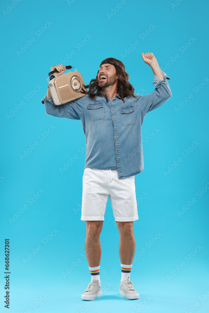 Stylish hippie man with retro radio receiver dancing on light blue background Stylish hippie man with retro radio receiver dancing on light blue background