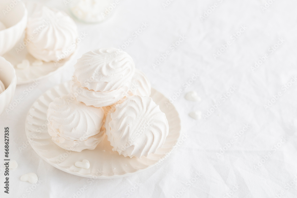 White airy zephyr or marshmallow shells on a plate on a white table, banner with space for text White airy zephyr or marshmallow shells on a plate on a white table, banner with space for text