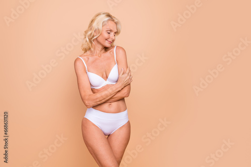 Perfect tone slender blonde hair gorgeous retired woman undressed embraces herself comfortable bath isolated on beige color background