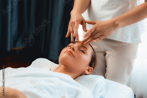 Caucasian woman enjoying relaxing anti-stress head massage and pampering facial beauty skin recreation leisure in dayspa modern light ambient at luxury resort or hotel spa salon. Quiescent