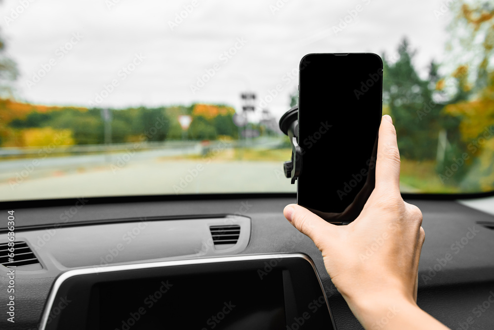 Hand putting mobile phone on car phone holder on windshield.