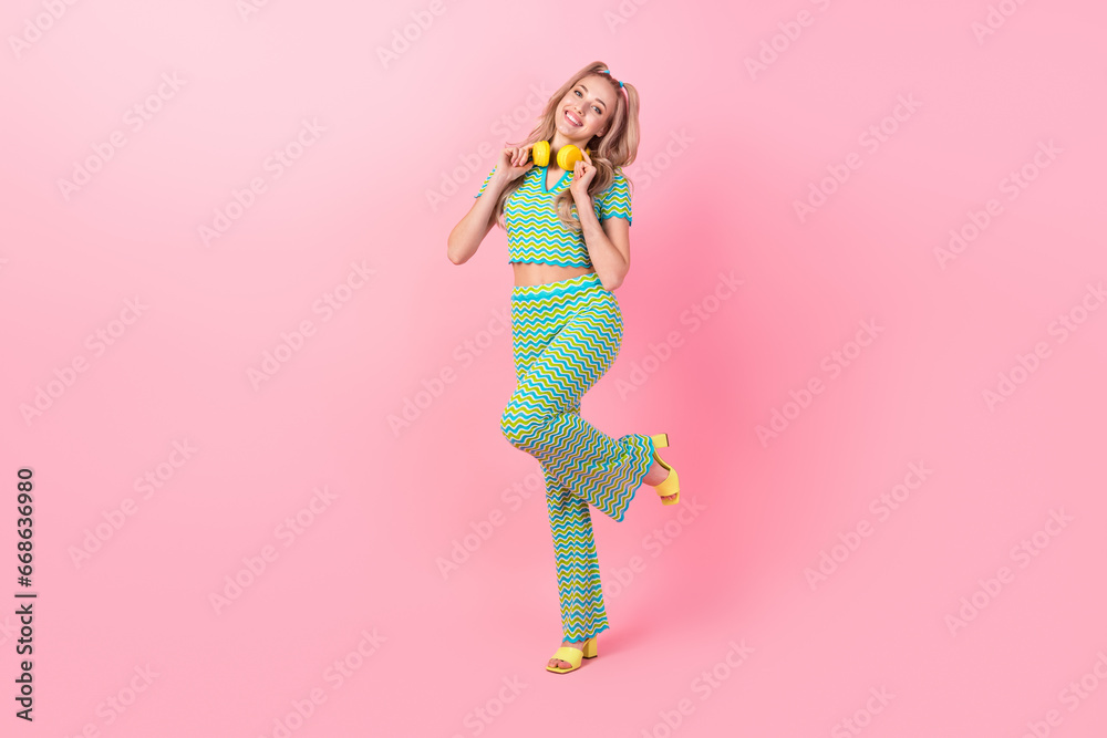 Full length photo of lovely young lady earphones look empty space dressed stylish green print garment isolated on pink color background Full length photo of lovely young lady earphones look empty space dressed stylish green print garment isolated on pink color background