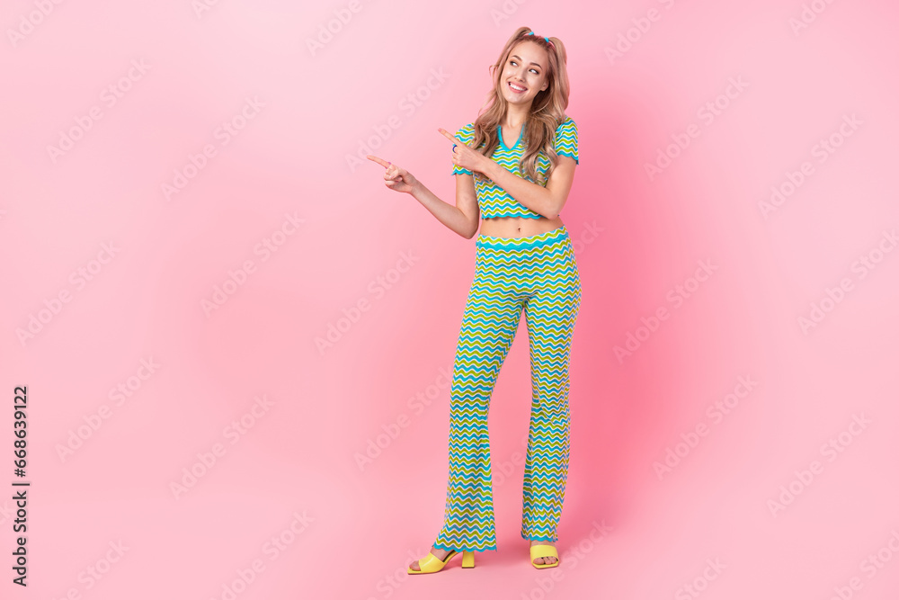 Full length photo of lovely young lady fingers point look empty space dressed stylish green print garment isolated on pink color background Full length photo of lovely young lady fingers point look empty space dressed stylish green print garment isolated on pink color background