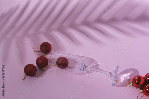 Creative tropical New Year party background with glass, Christmas baubles, and palm shadow. Party background idea. Flat lay.
