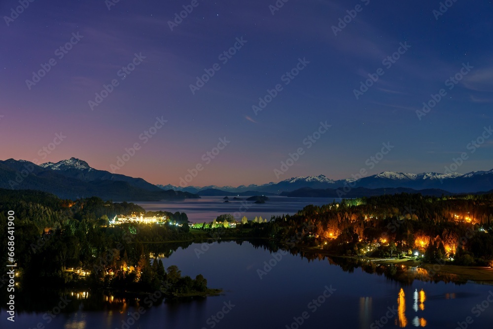 lake surrounded by forest and mountains at dusk with the moon in the sky