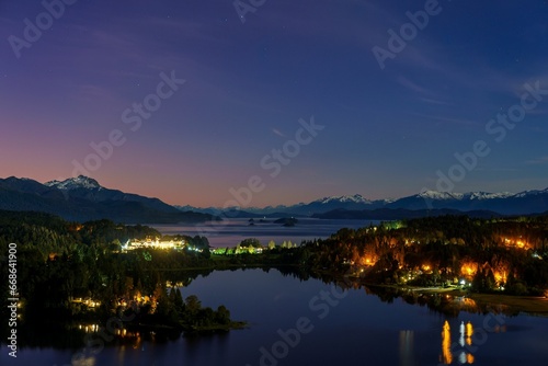 lake surrounded by forest and mountains at dusk with the moon in the sky photo