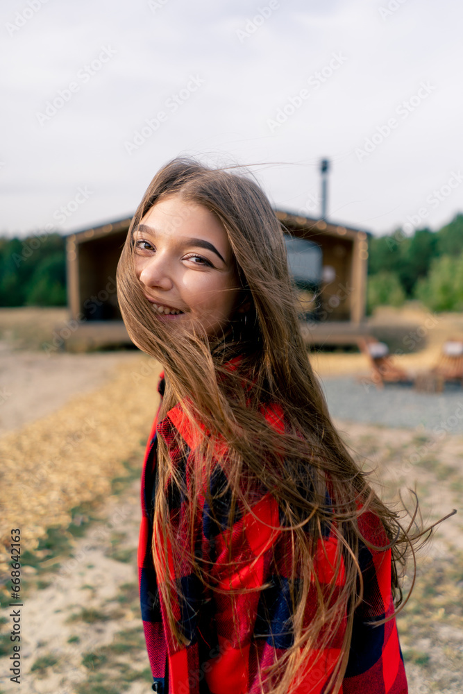 Fototapeta premium Close-up portrait of the face of a beautiful girl who runs to wooden cabin in woods and looks back